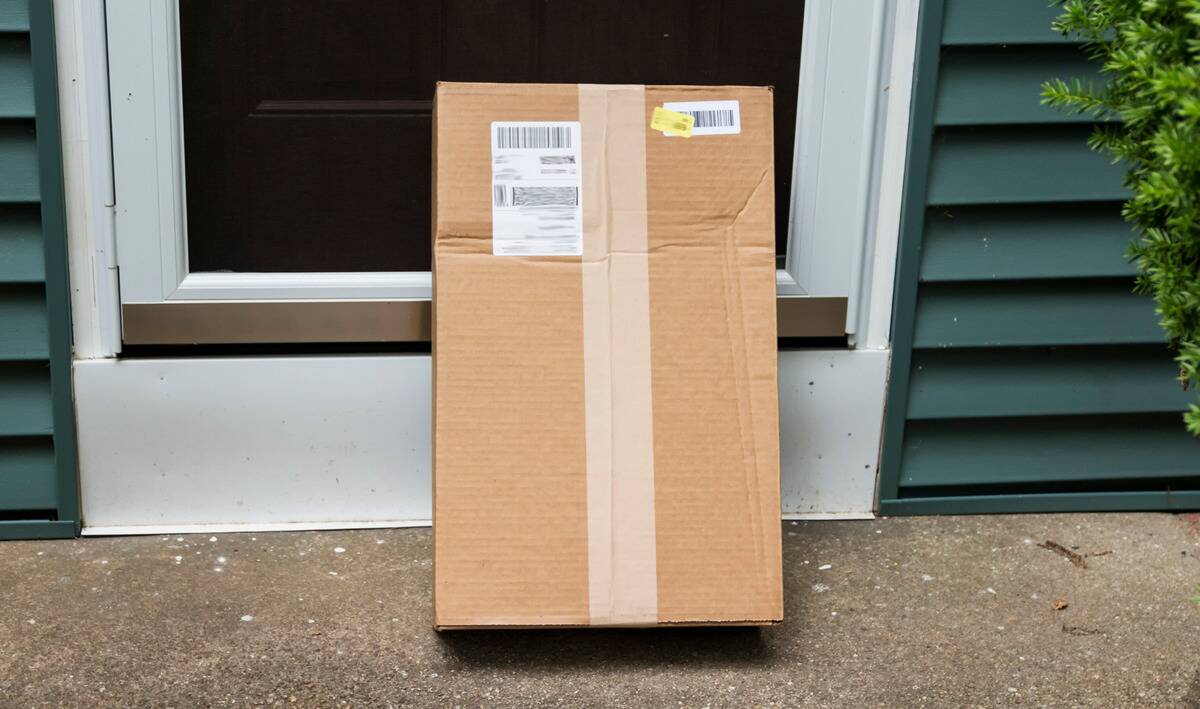 A large package stood vertically in front of a door on a concrete porch.