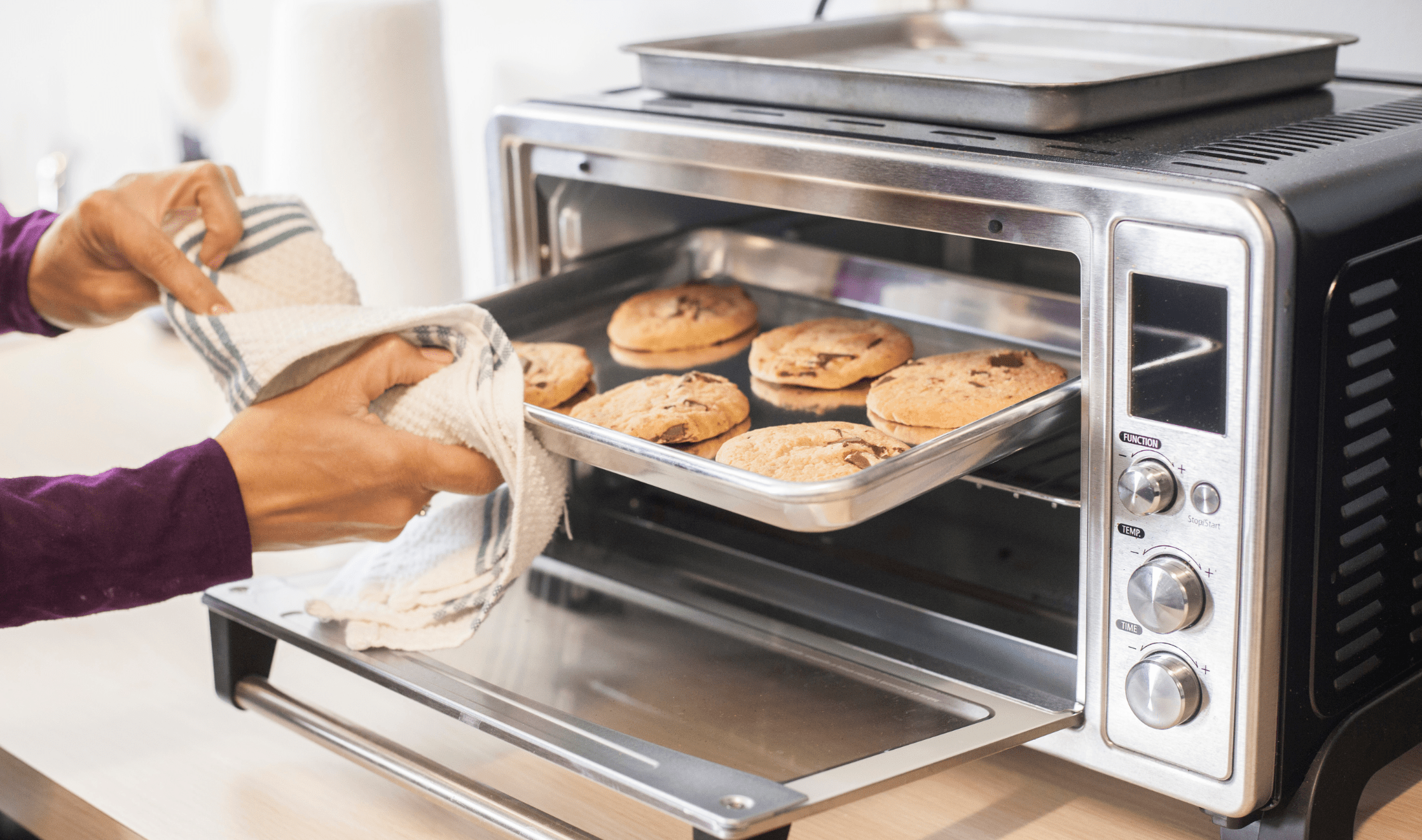 A person pulling cookies out of a toaster oven.