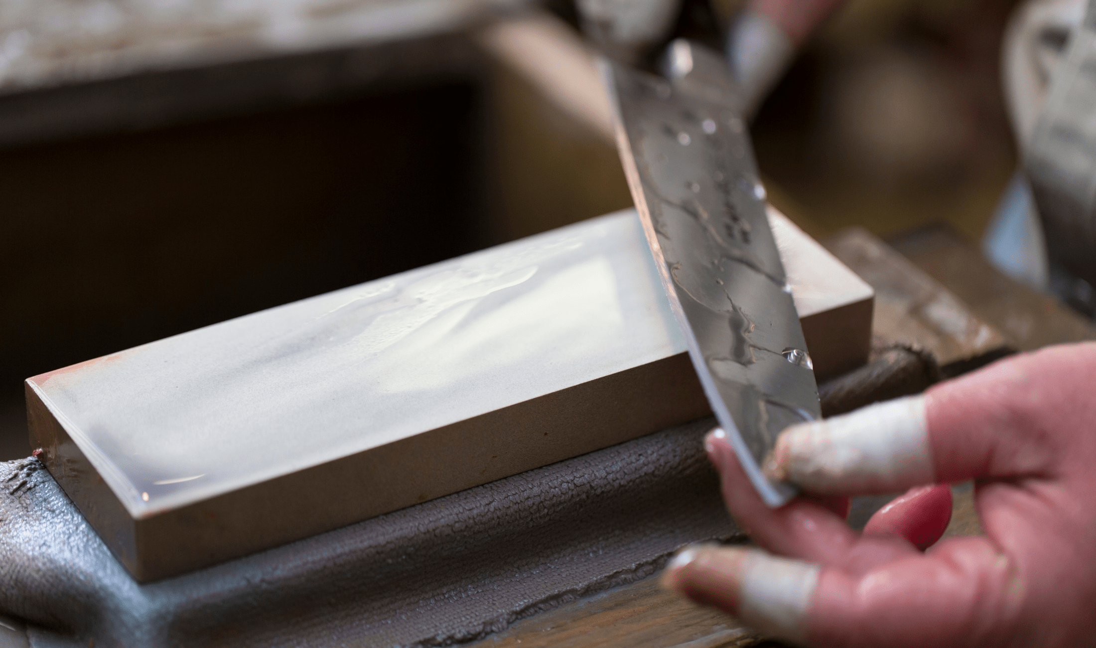 A closer photo of someone using a whetstone to sharpen a knife.