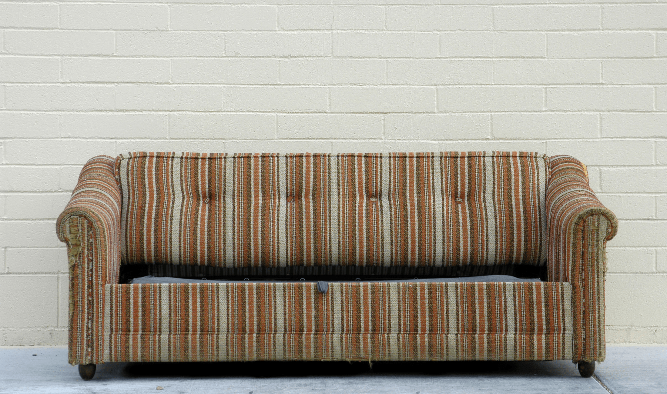 An old couch sitting against a bare wall.