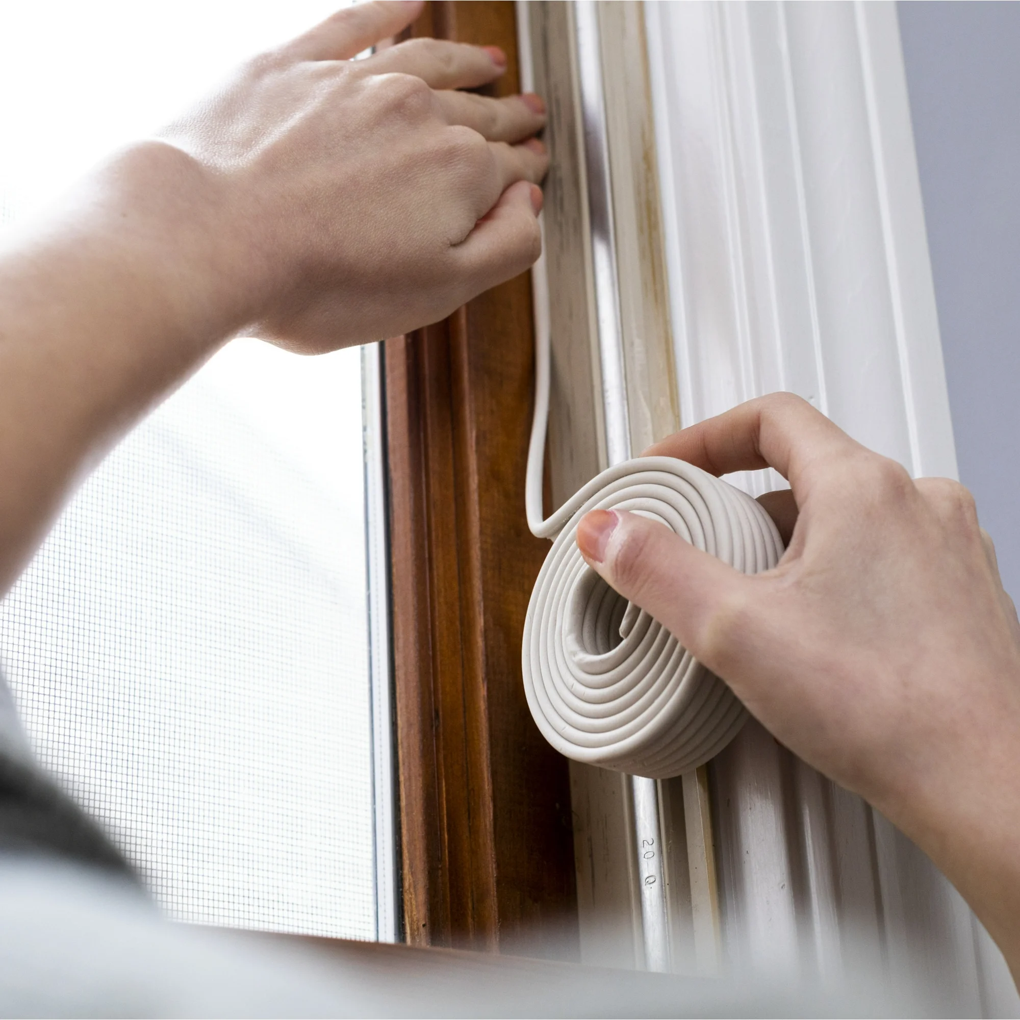 A person fitting rope caulk into the corners of their windows.